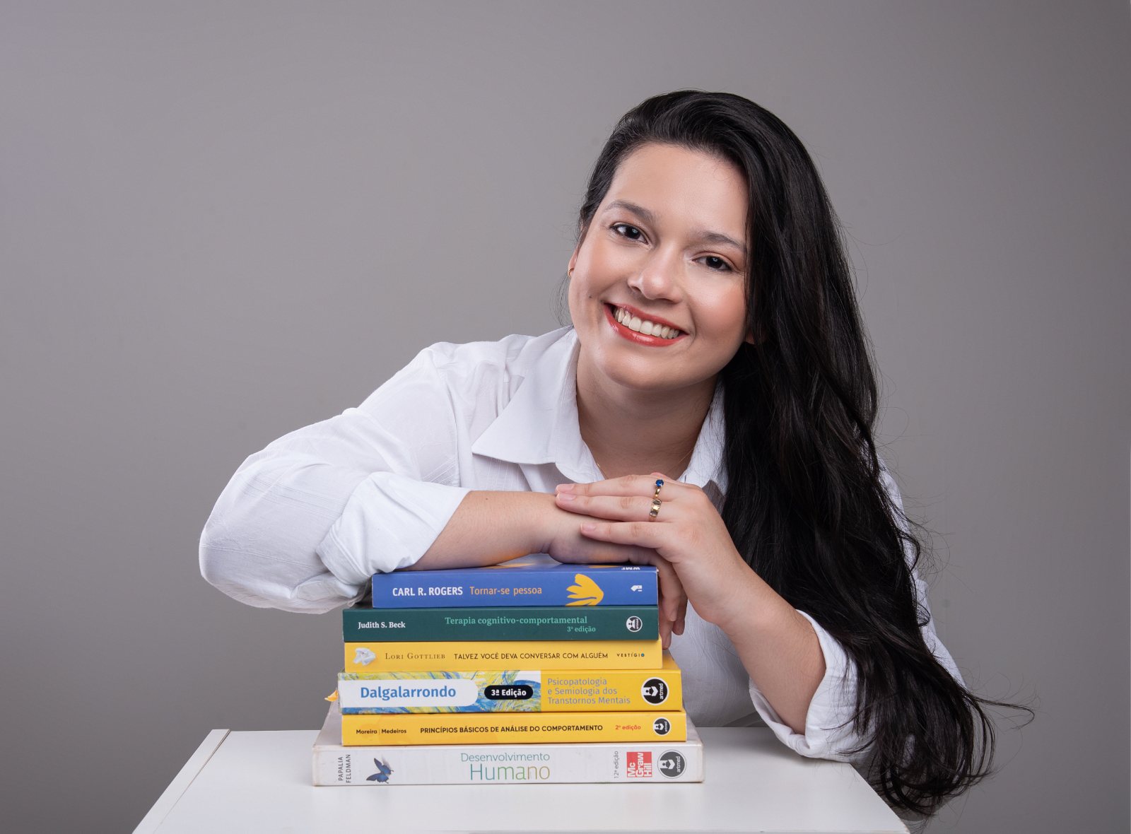 Karine Lima sorrindo, apoiada sobre uma pilha de livros